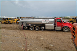 A John Moore Oil Company fuel delivery truck making a delivery at a job site with construction equipment around it